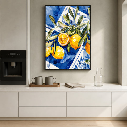 A framed vertical canvas print featuring a vibrant blue and white watercolor-style painting of oranges and green leaves, hanging on a light gray wall above a white kitchen counter with mugs and a glass carafe.