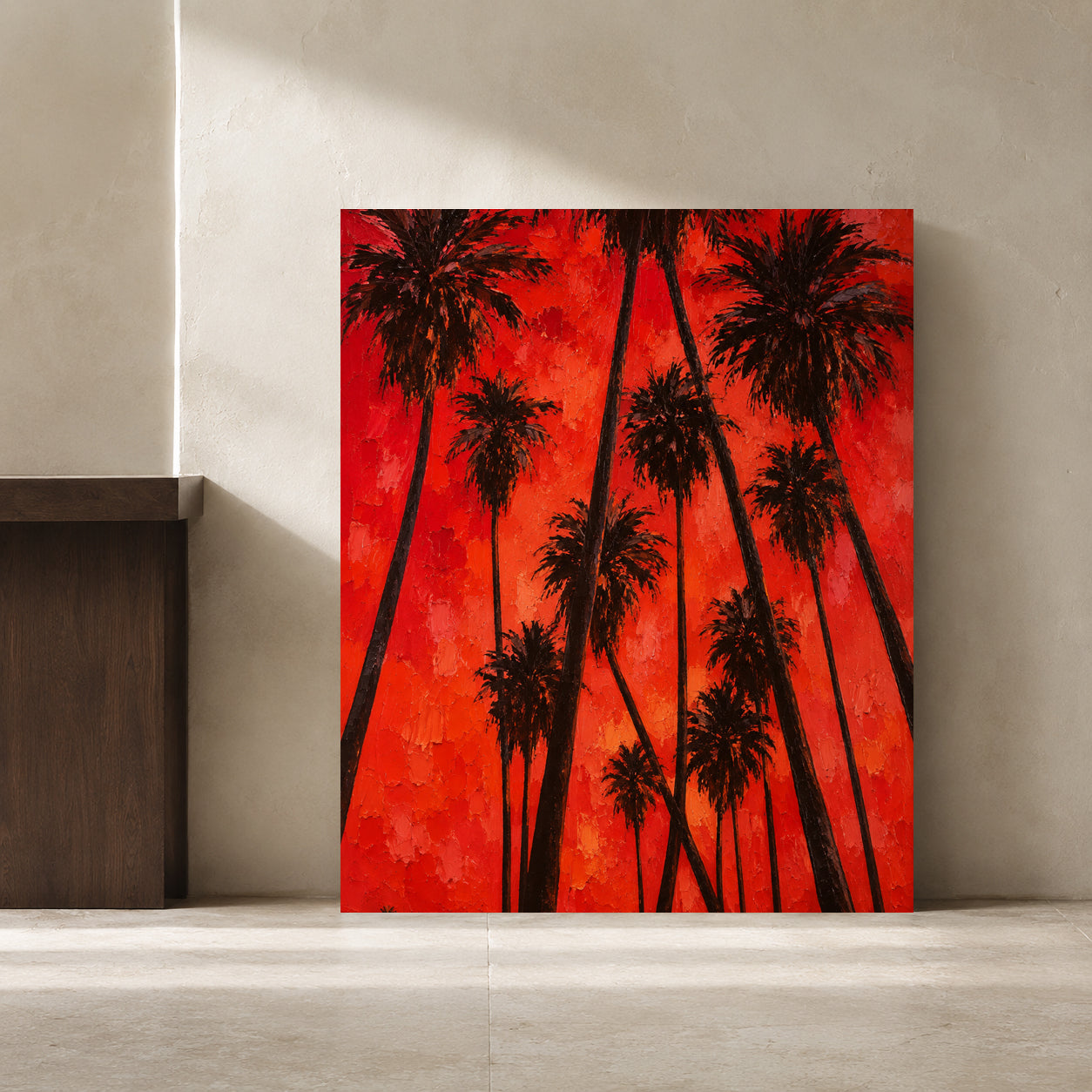 A vertical canvas painting of black palm tree silhouettes against a vibrant red and orange textured background, leaning against a neutral concrete wall.