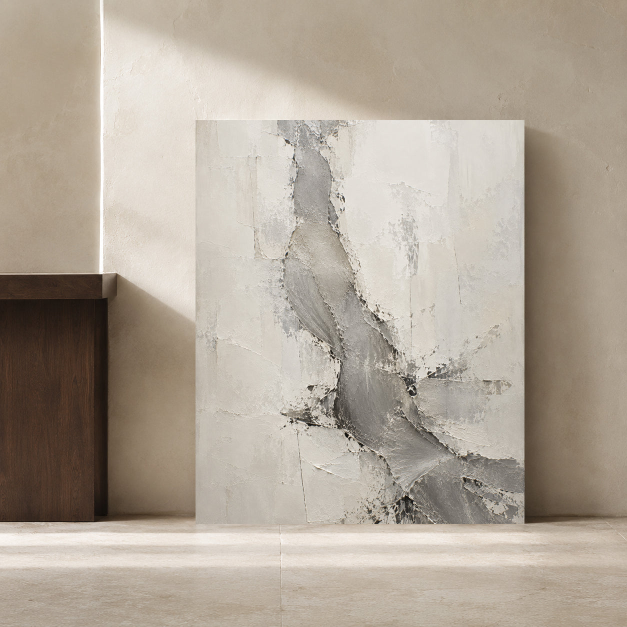 An abstract canvas painting with textured gray and off-white brushstrokes, leaning against a beige plaster wall in a minimalist interior setting.