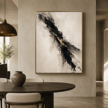 Abstract framed wall art hanging in a modern dining room. The artwork features a diagonal black and gray brushstroke pattern with a touch of gold on a warm off-white background, enclosed in a thin gold frame.