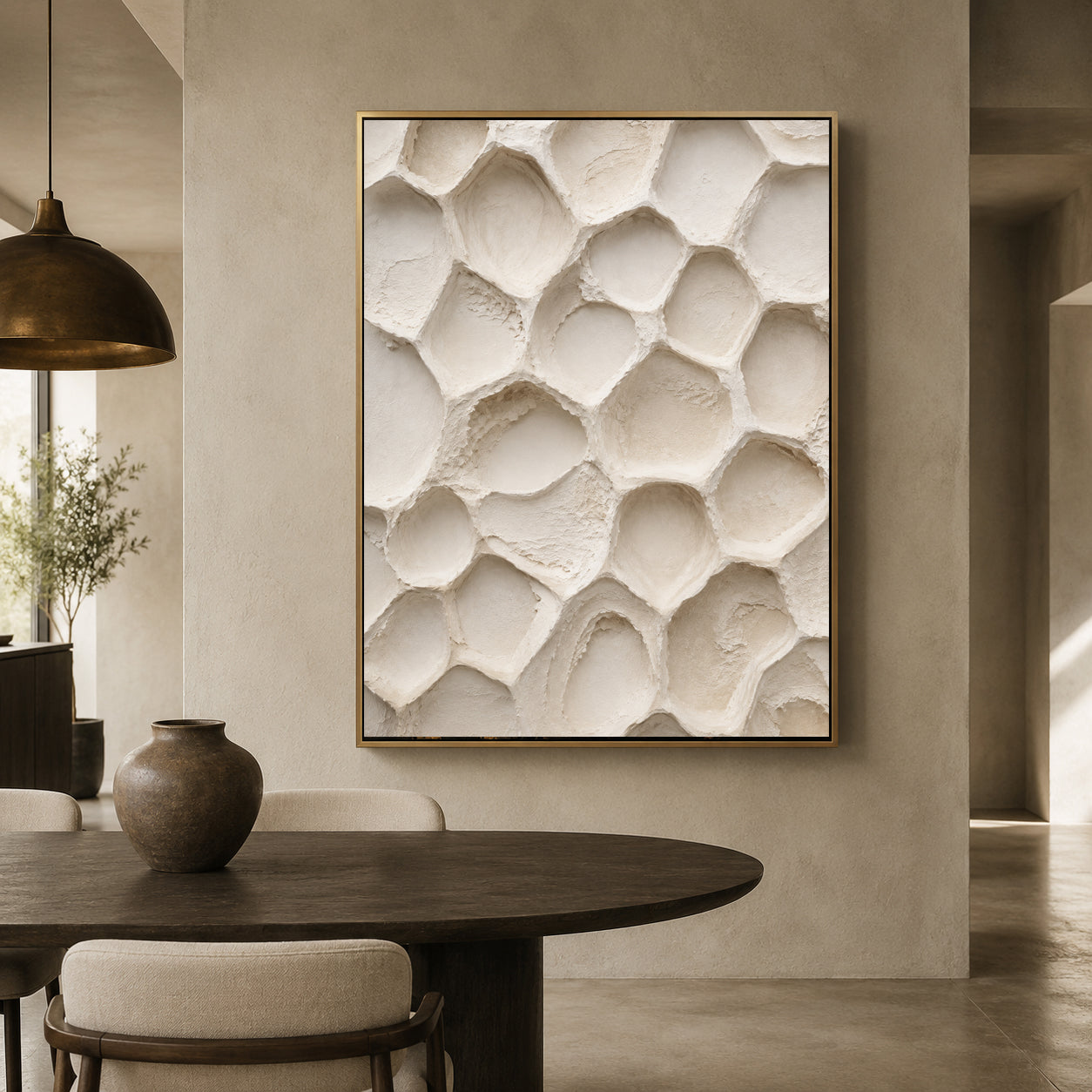 A framed wall art print featuring a textured, organic honeycomb-like pattern in warm off-white tones, hanging on a beige plaster wall above a dark wood dining table in a modern, minimalist interior.
