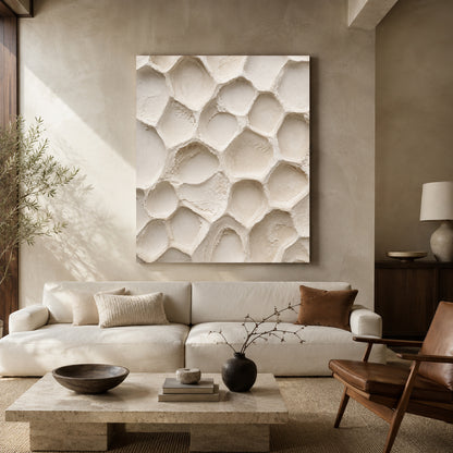 Large square canvas wall art featuring a textured organic pattern in warm off-white and beige, displayed above a cream sofa in a modern, neutral-toned living room.
