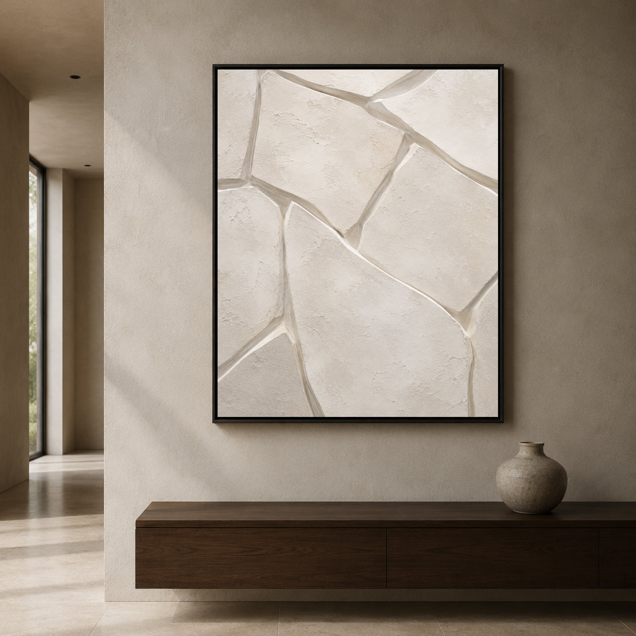 A framed abstract wall art print featuring textured beige stone-like shapes with gray fissures, displayed in a minimalist interior setting above a dark wood console table.