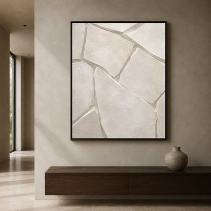A framed abstract wall art print featuring textured beige stone-like shapes with gray fissures, displayed in a minimalist interior setting above a dark wood console table.