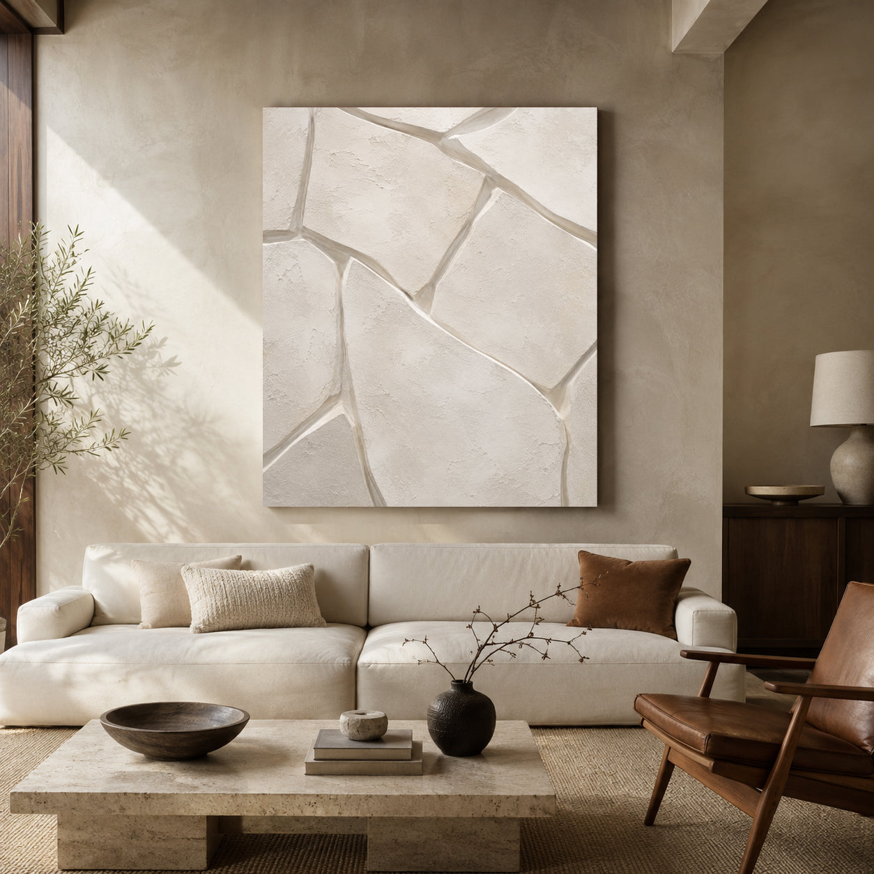 Large square abstract wall art with a cracked stone or concrete pattern in warm off-white and beige tones, displayed above a cream sofa in a styled living room.