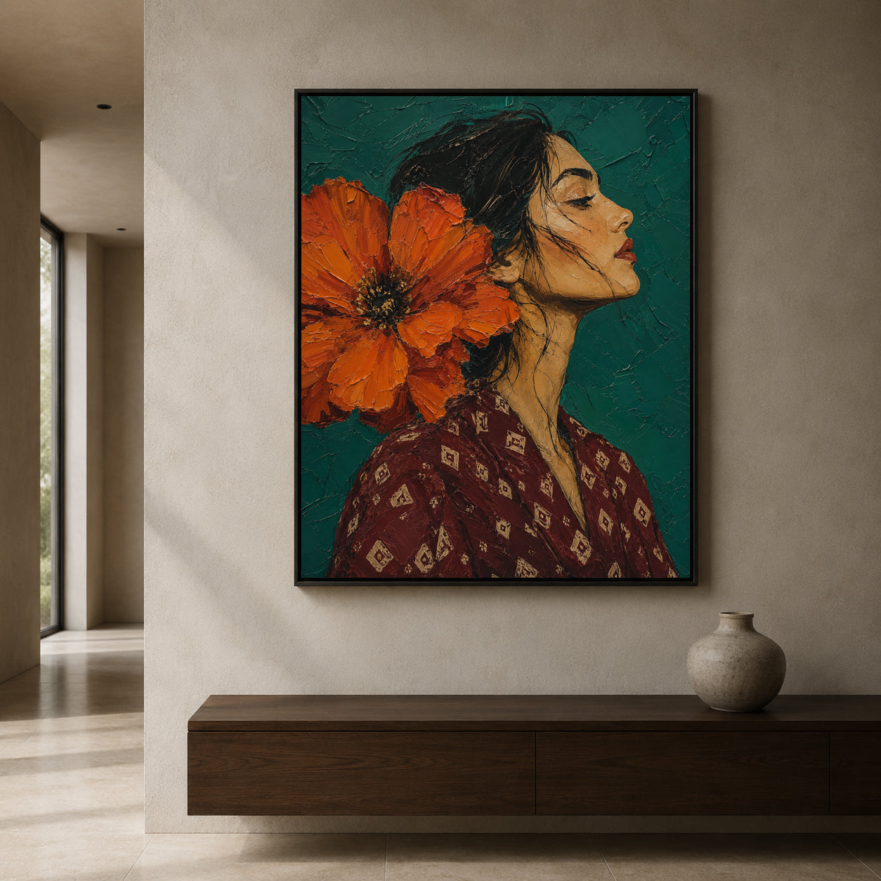 A framed vertical art print depicting a woman in profile with a large orange flower on her head, hanging on a beige wall above a dark wood console with a ceramic vase.