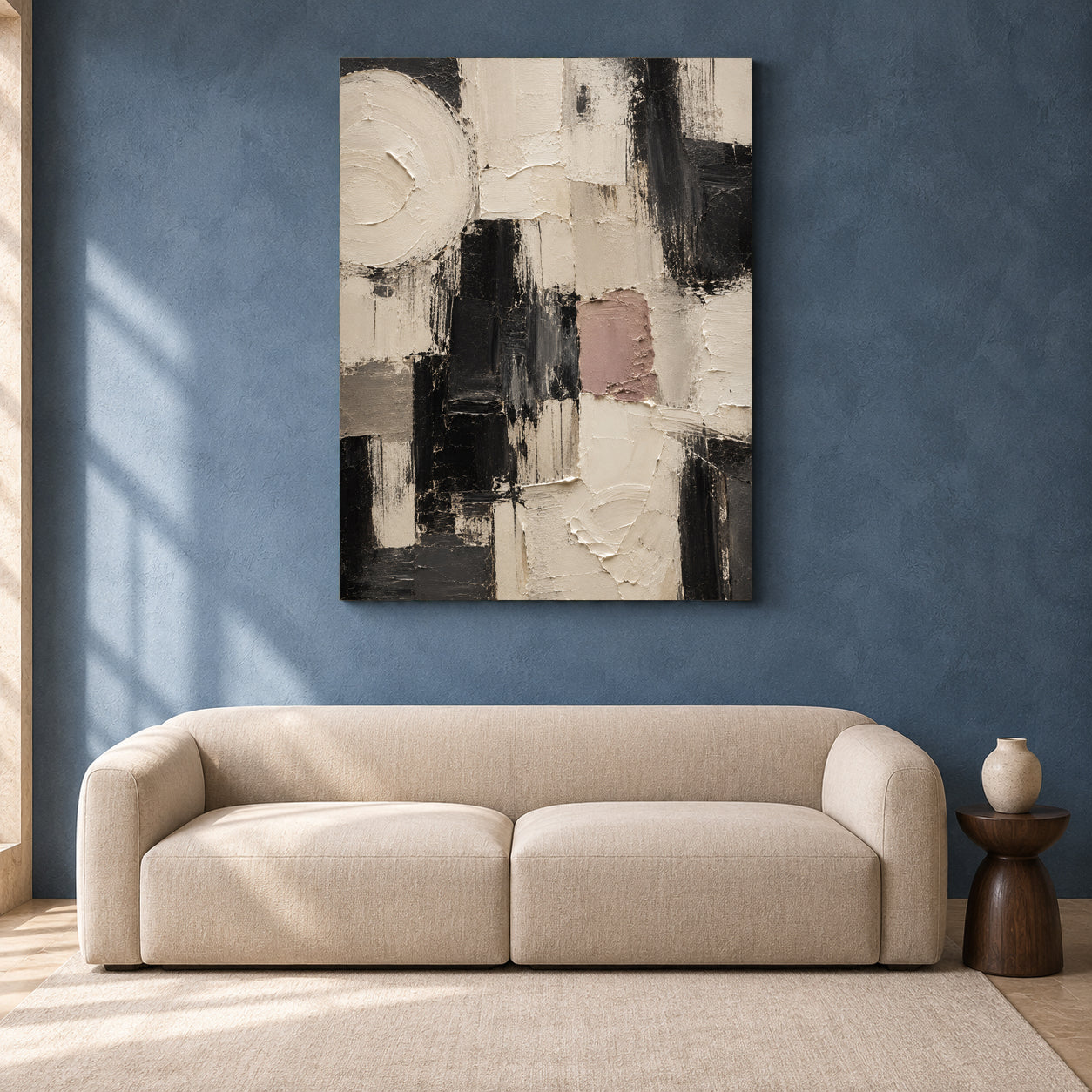 An abstract canvas wall art print with black, white, beige, and dusty pink brushstrokes, displayed on a textured blue wall above a modern beige sofa.