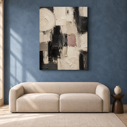 An abstract canvas wall art print with black, white, beige, and dusty pink brushstrokes, displayed on a textured blue wall above a modern beige sofa.