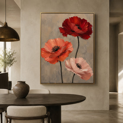 A framed wall art print featuring three large poppy flowers in red, orange, and pale pink on a textured gray background, displayed above a dark wood dining table in a modern interior setting.