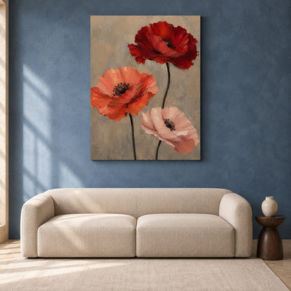 A vertical canvas wall art print featuring three textured poppy flowers in red, orange, and soft pink on a warm beige background, displayed in a modern living room setting above a beige sofa against a textured blue wall.
