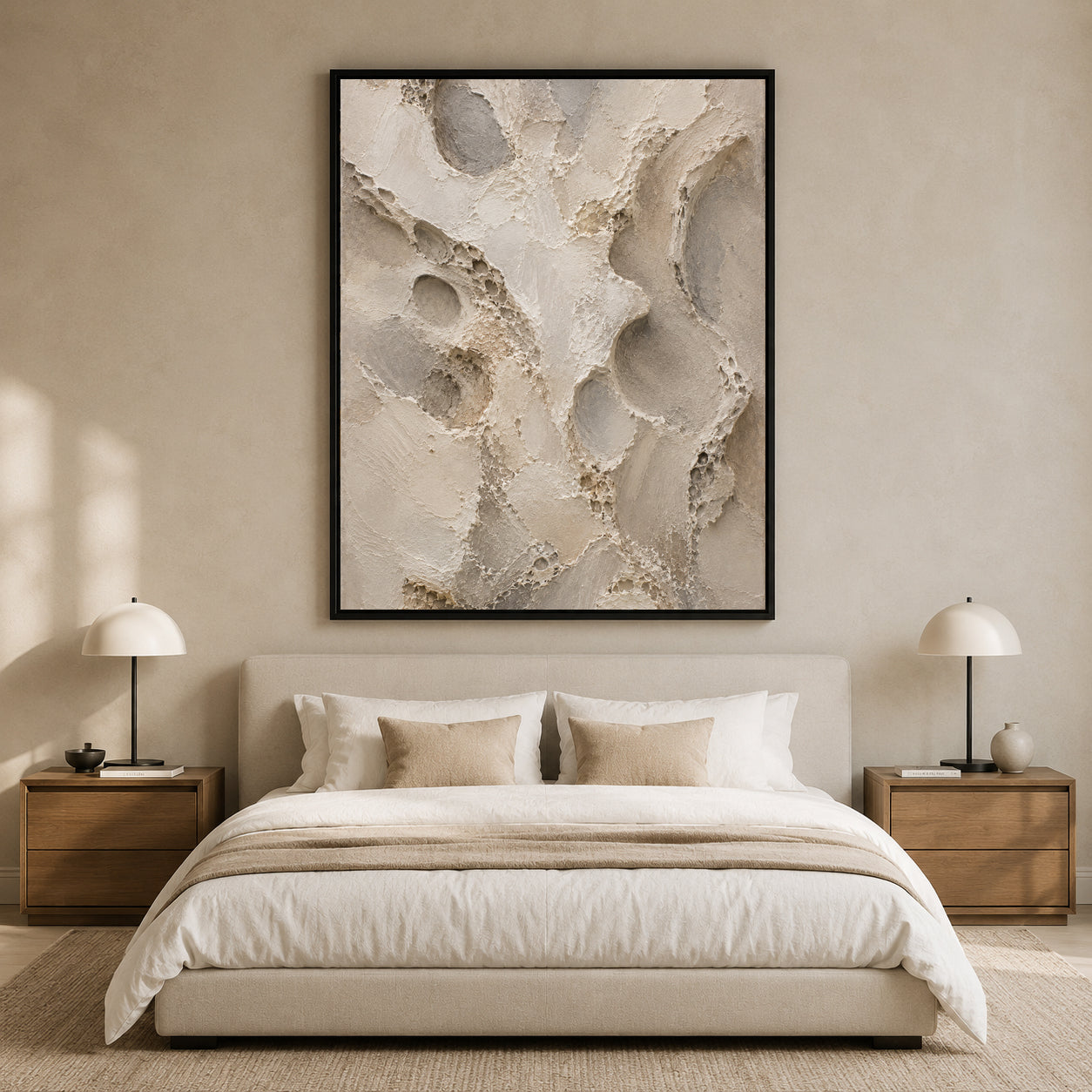 A large framed abstract wall art print with textured beige, cream, and gray brushstrokes hangs above a neatly made bed in a minimalist, warm-toned bedroom.
