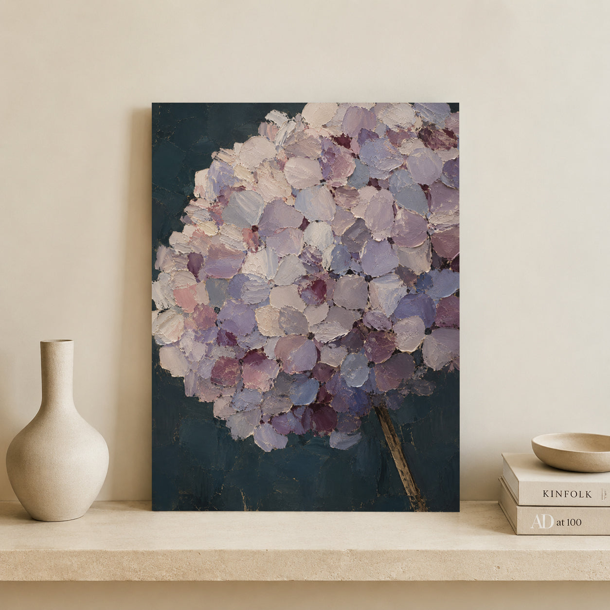 A vertical canvas art print featuring an impressionistic painting of a lavender hydrangea with textured brushstrokes in shades of purple, lilac, and white against a dark teal-blue background. The canvas is styled on a beige stone shelf next to a ceramic vase and books.