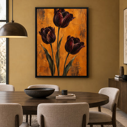 A framed vertical canvas print of three dark burgundy tulips on a textured orange background, hanging on a warm mustard-yellow wall above a wooden dining table with upholstered chairs.