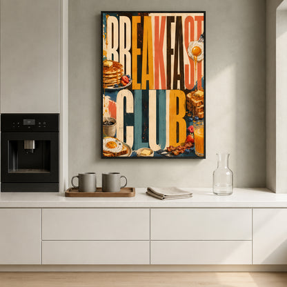 A framed vertical wall art print with a colorful collage-style breakfast theme hangs on a light gray kitchen wall above a white countertop. The print features large text reading 'BREAKFAST CLUB' with pancakes, eggs, toast, and other breakfast imagery.