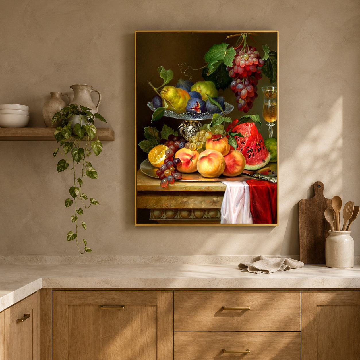 A framed still life wall art print depicting a fruit table scene with grapes, peaches, pears, watermelon, and a glass of red wine, displayed above a kitchen counter in a warm beige interior.