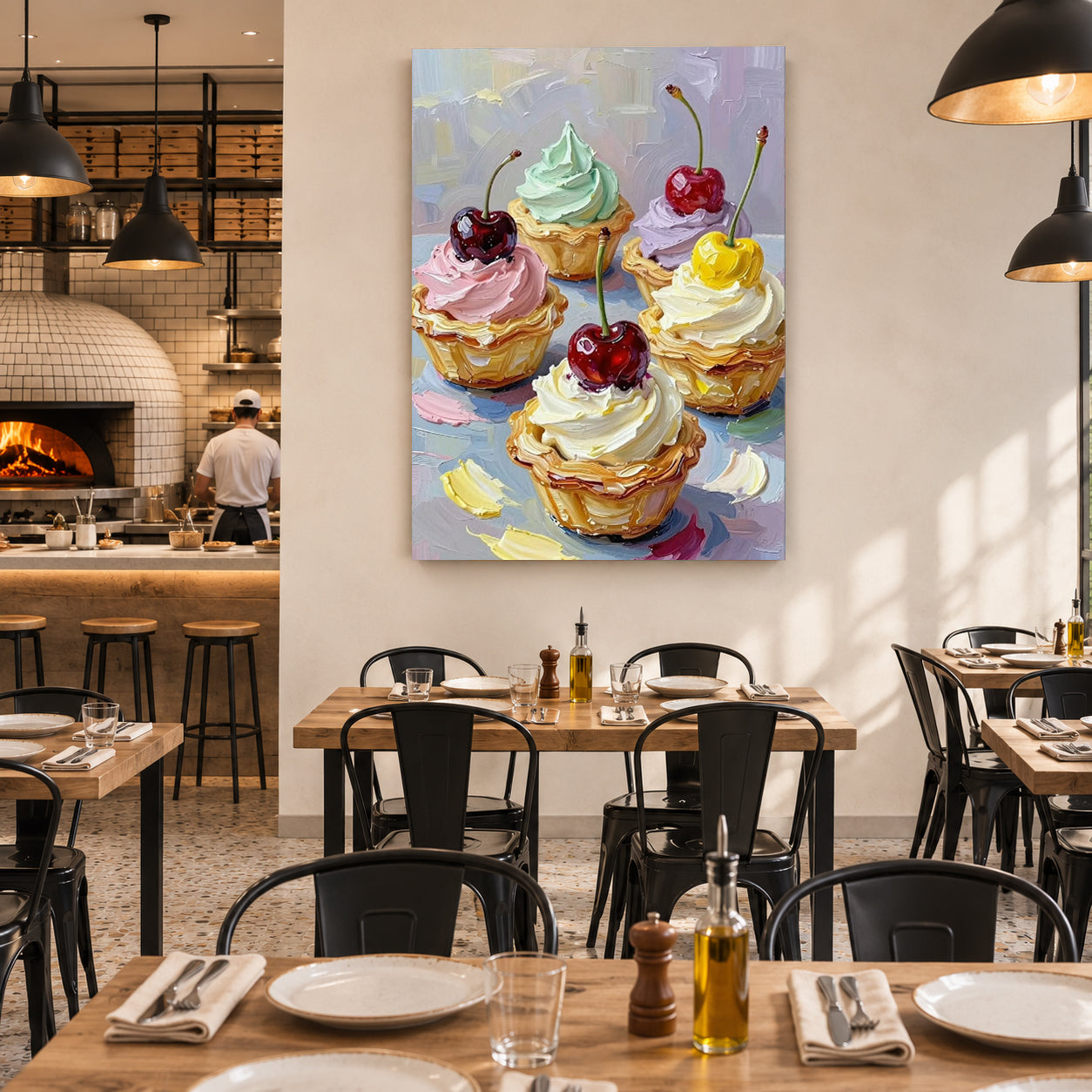 A colorful canvas wall art print depicting four decorated cupcakes with cherries, displayed on a beige wall in a modern restaurant setting with wooden tables and black chairs.