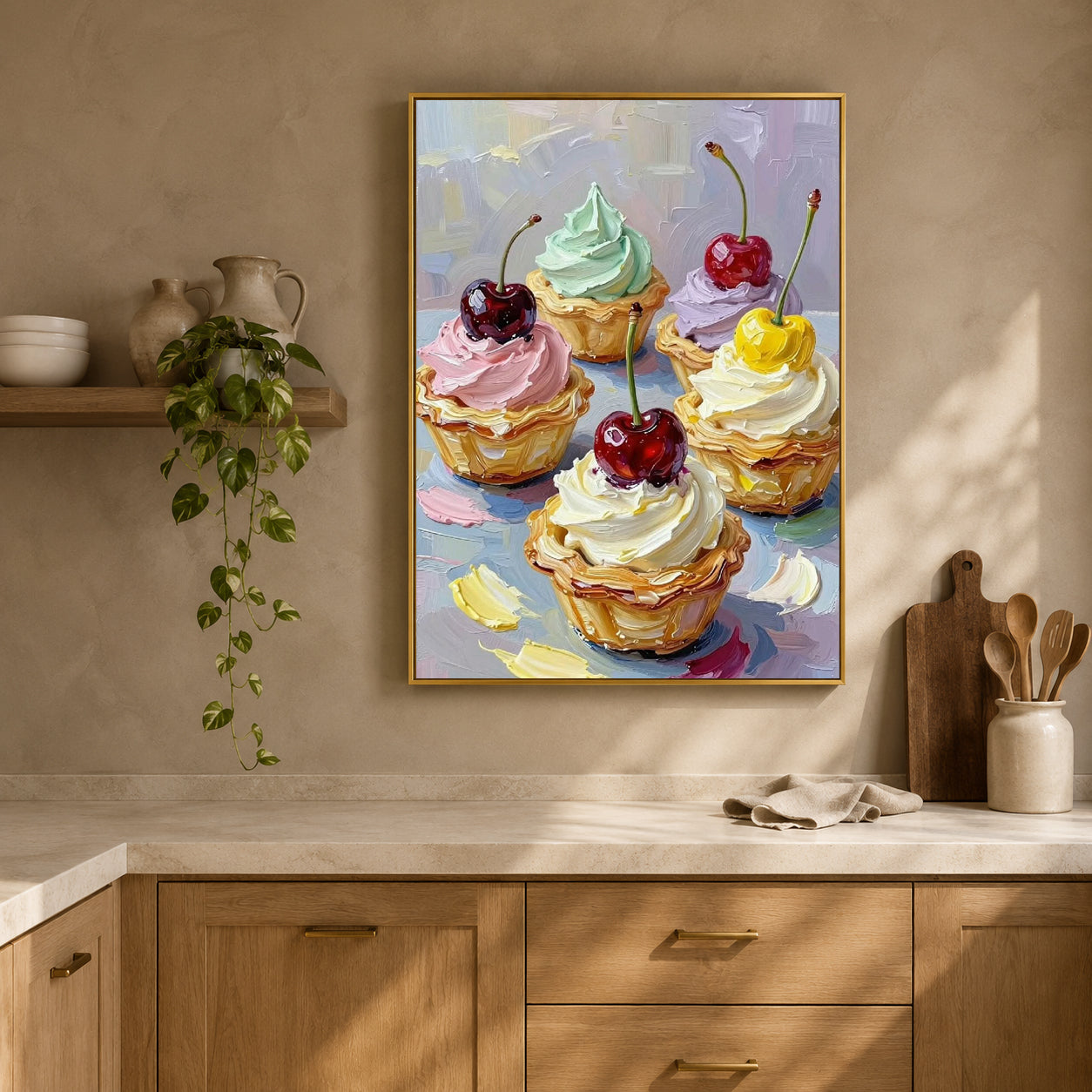 A framed colorful painting of six iced cupcakes with cherries, hanging on a beige wall above a kitchen counter with a plant and wooden utensils.