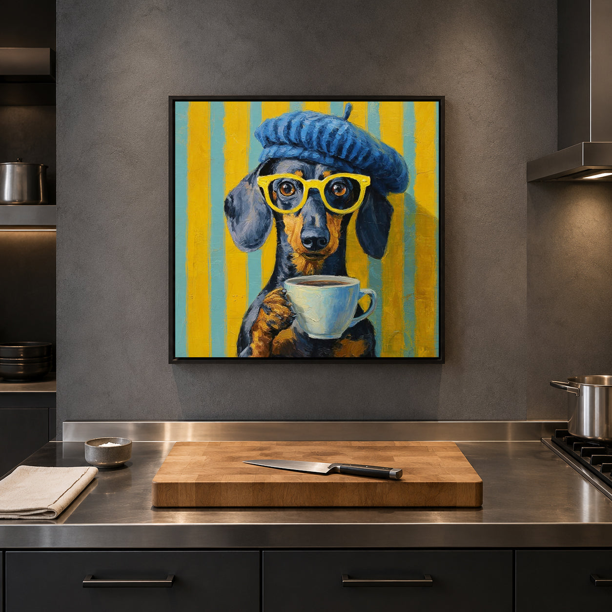 A framed square wall art print depicting a dachshund wearing a blue beret and yellow glasses while holding a white coffee mug, set against yellow and blue vertical stripes. The artwork is displayed on a dark gray kitchen wall above a stainless steel counter with a wooden cutting board and knife.