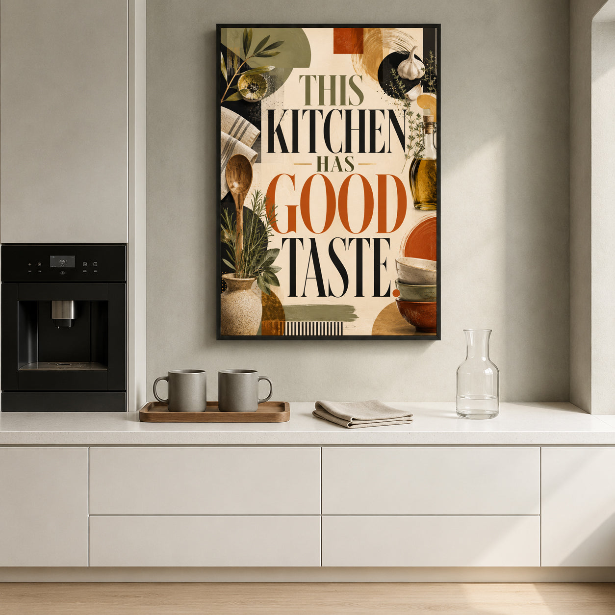 A framed kitchen art print with the text 'THIS KITCHEN HAS GOOD TASTE' hangs on a light gray wall above a white countertop in a modern kitchen setting.
