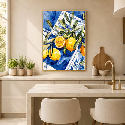 A vertical framed canvas print featuring a vibrant blue and white watercolor-style illustration of oranges with green leaves, hanging on a beige wall in a modern kitchen setting.