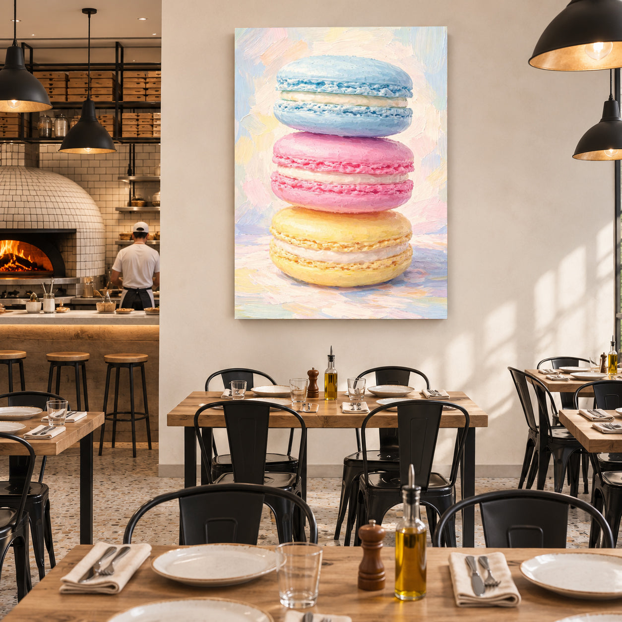 A vertical canvas wall art print depicting three colorful macarons (blue, pink, and yellow) on a pastel background, displayed on a dining room wall above a wooden table in a modern restaurant setting.