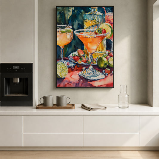 A framed vertical watercolor painting of colorful cocktails, fruit, and a bottle hanging on a light gray wall above a white kitchen counter with mugs, a glass carafe, and a coffee machine.